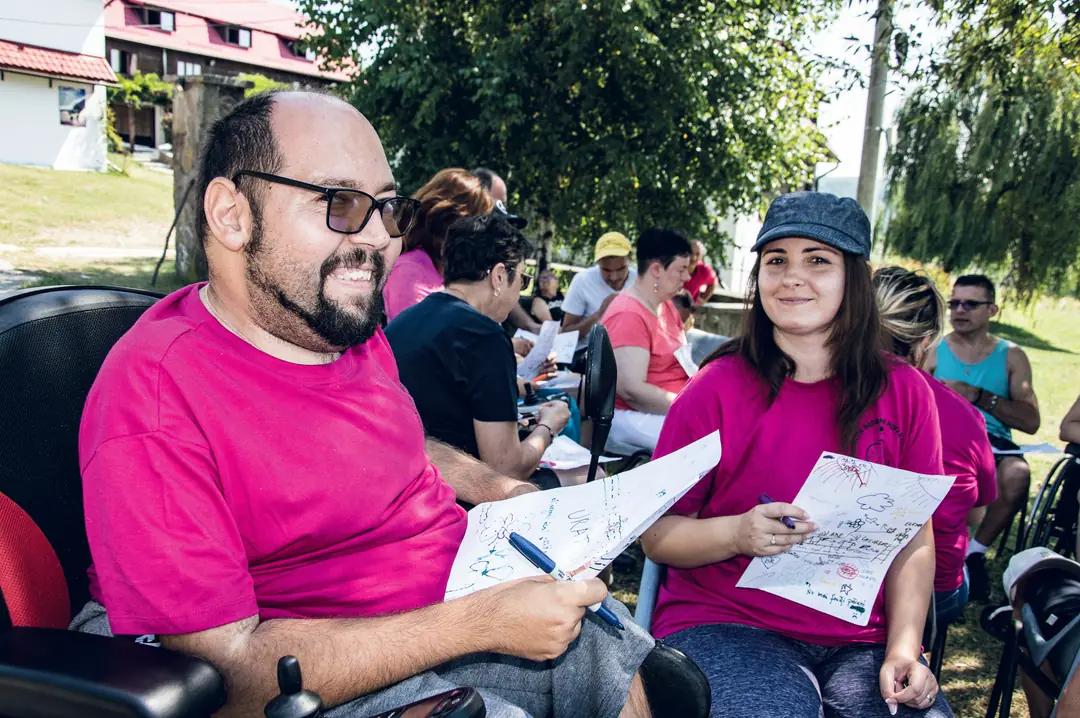 A man and a woman in magenta T-shirts, holding drawings