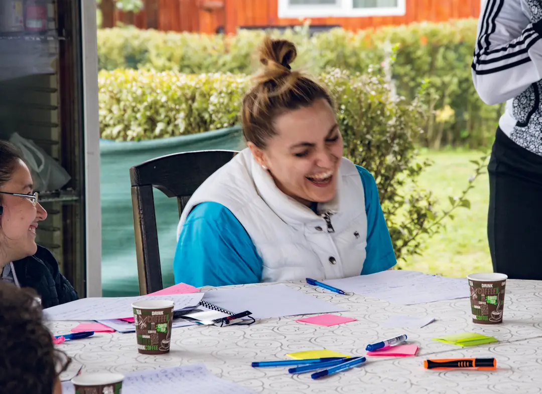 A woman laughing at a table covered with paper and markers