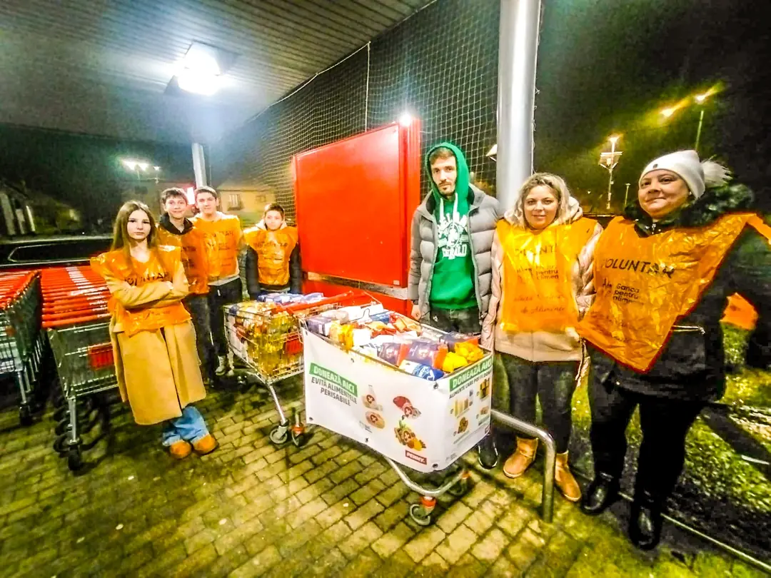 Narancssárga mellényes önkéntesek egy élelmiszerrel teli kosár mellett