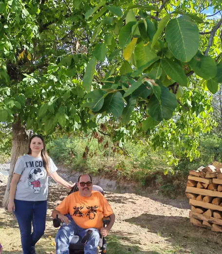 A man in a wheelchair and a woman under a walnut tree