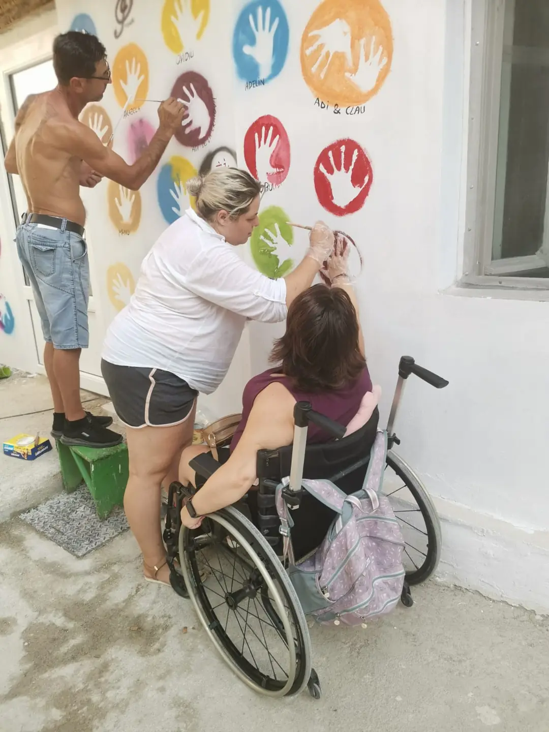 Three people painting colorful prints on a wall