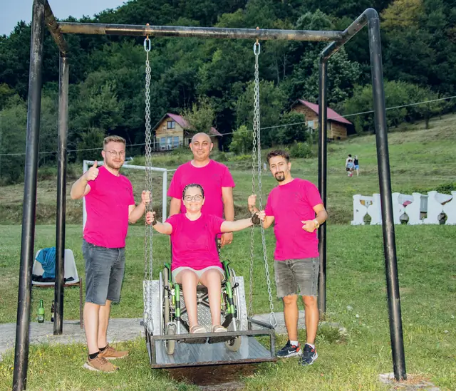 Egy résztvevő a kerekesszékes hintán, mellette három önkéntes
